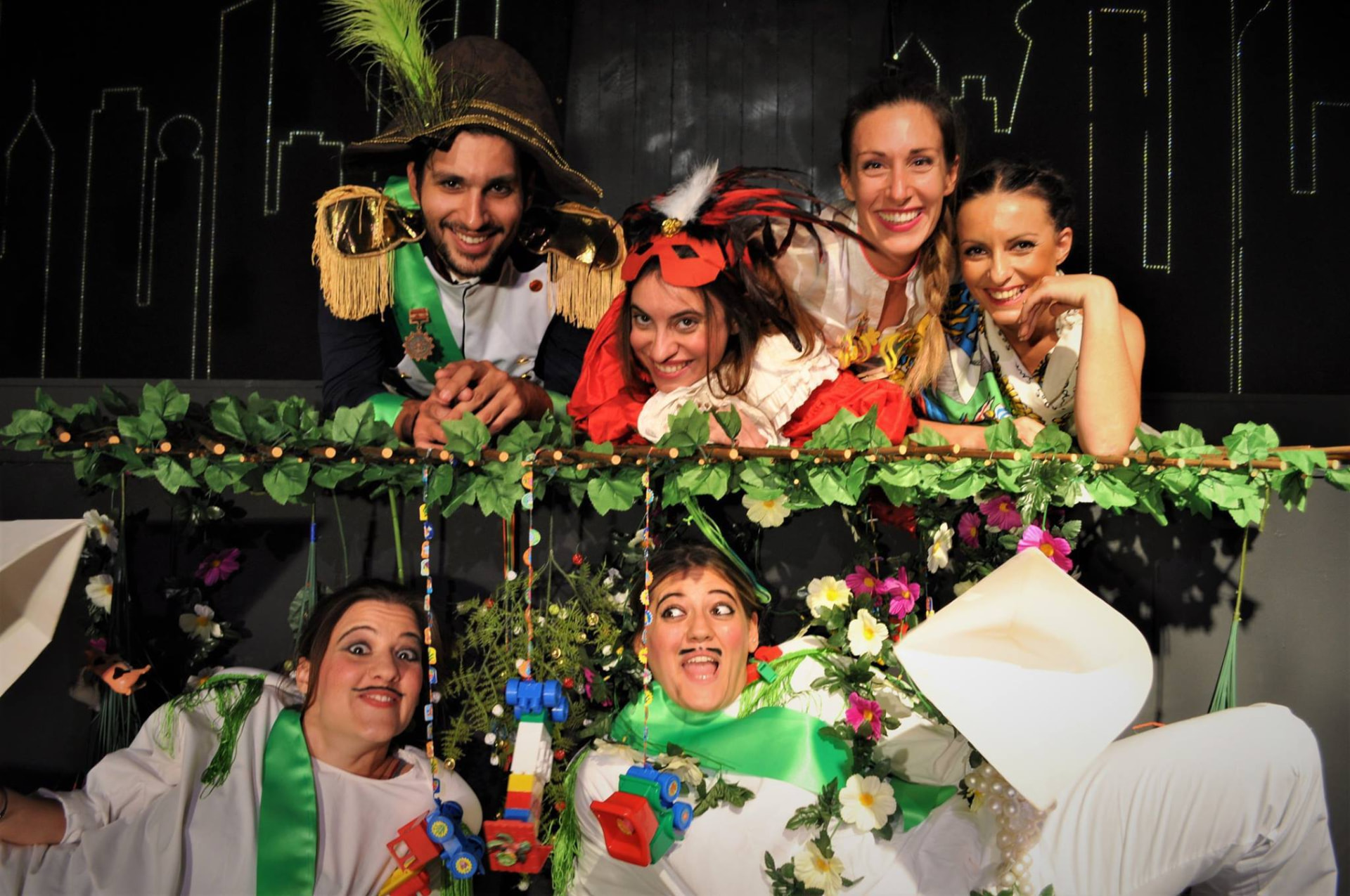 The company of Une ville, mais quelle ville in white and green costumes leaning over a garland